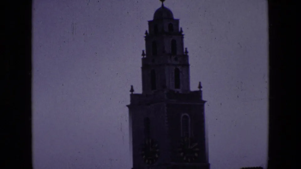 1969 Ireland 8mm frame showing a closer, darkened view of the clock tower with clock faces and weather vane visible.