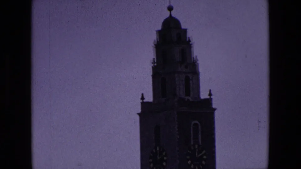 1969 Ireland 8mm frame showing a dark church or civic tower silhouette with clock faces against a dusky purple sky.