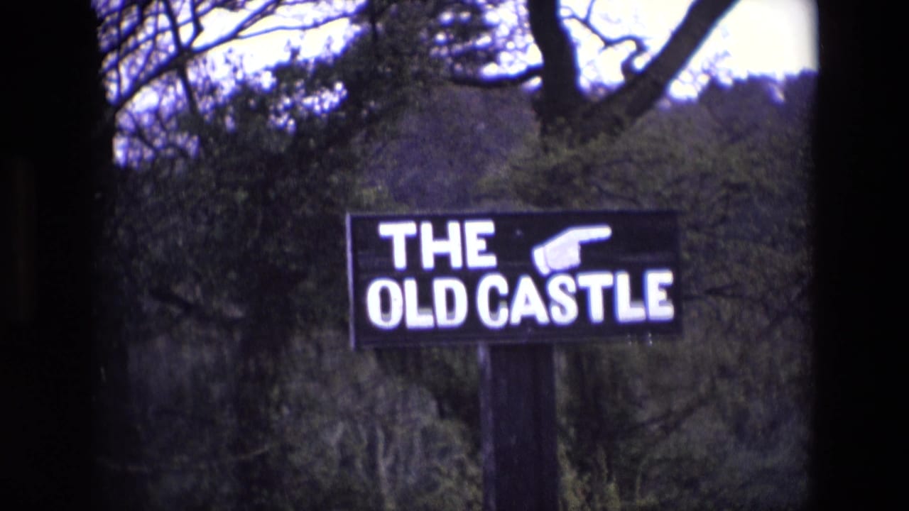 Black THE OLD CASTLE sign with white lettering in a wooded outdoor setting.