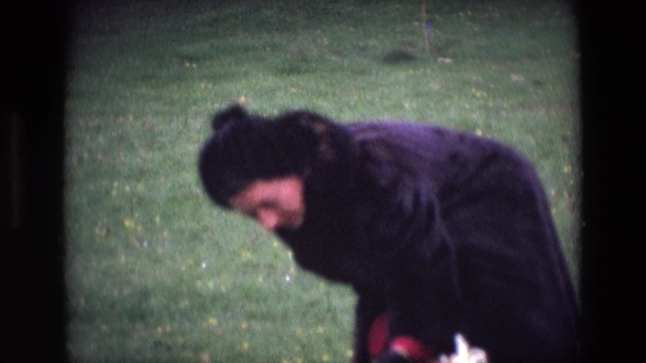 Woman in a dark coat bends over grass in a park.