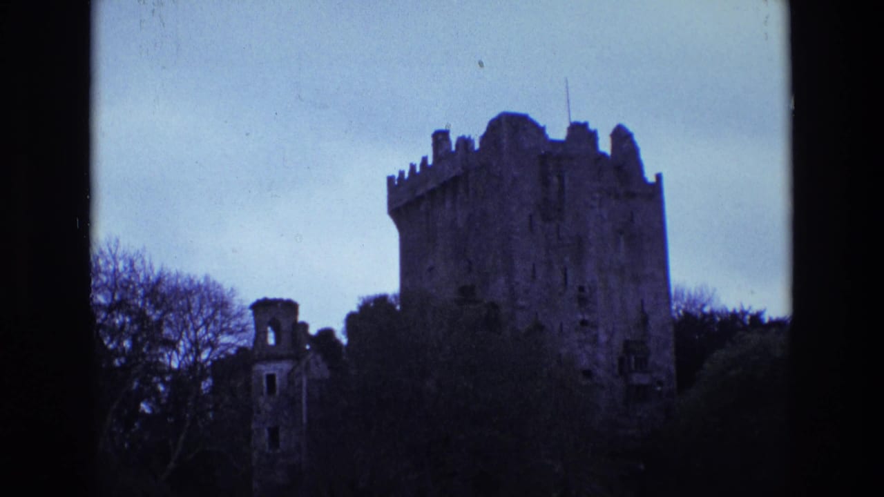 1969 Ireland home-movie frame of a shadowed stone castle and smaller ruined structure beneath a pale blue sky.