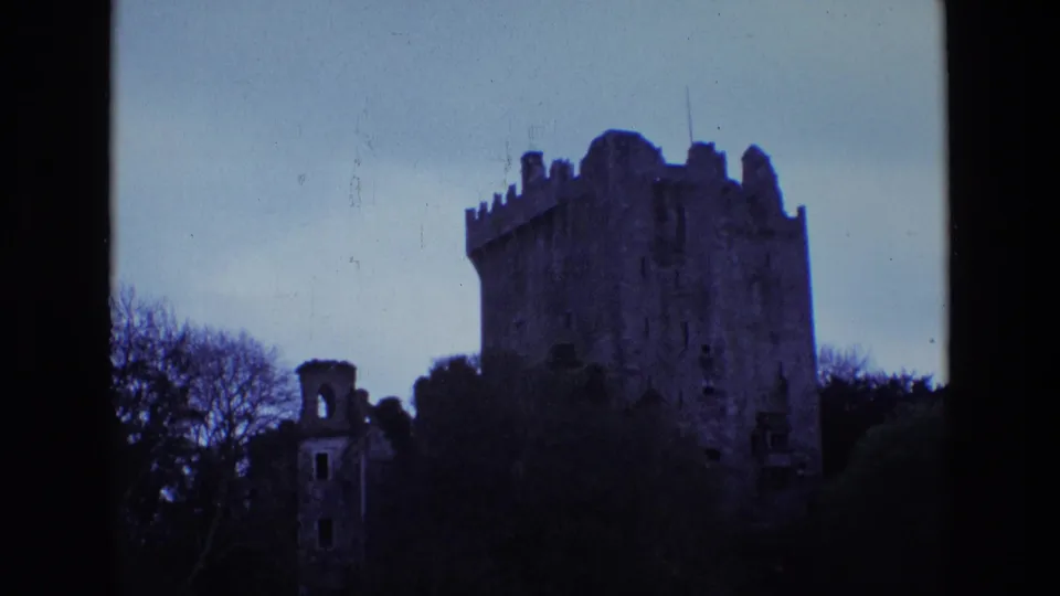 1969 Ireland 8mm frame showing a dim castle exterior, bare trees, dark vegetation, and visible film wear.