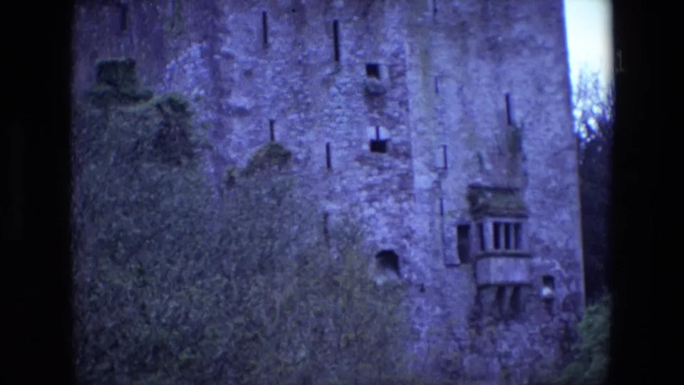 1969 Ireland 8mm frame showing the castle wall in closer detail, including ivy or brush, small openings, and a projecting balcony window.