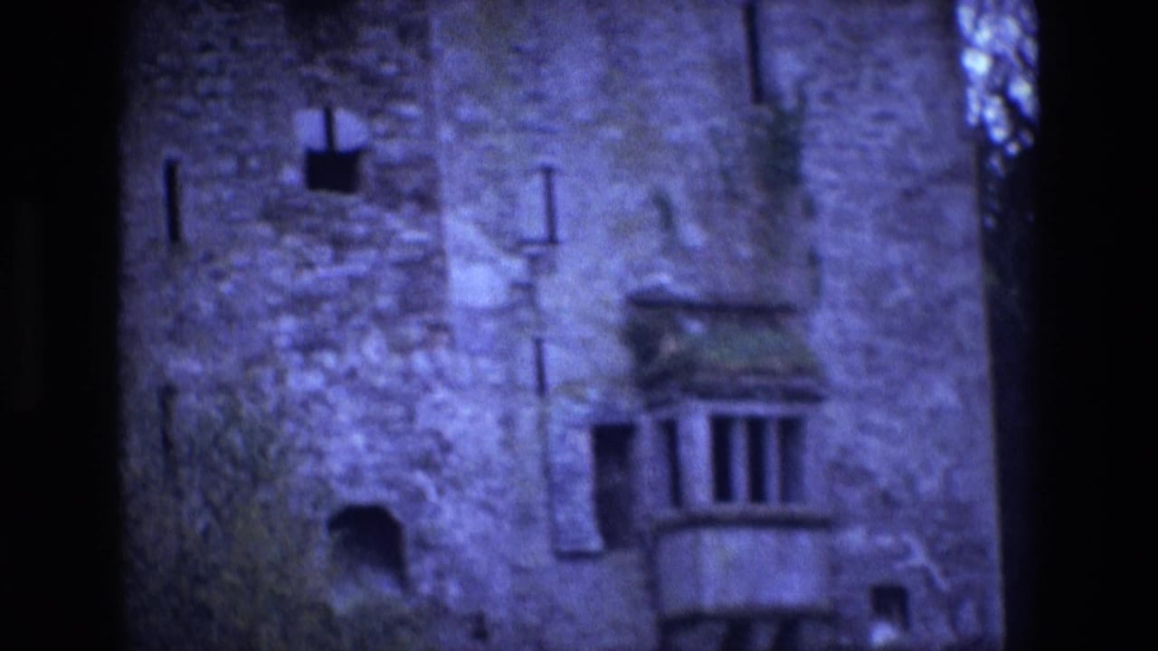 1969 Ireland 8mm frame of the castle exterior, with rough masonry, vertical narrow windows, a balcony-like projection, and soft blue-purple exposure.