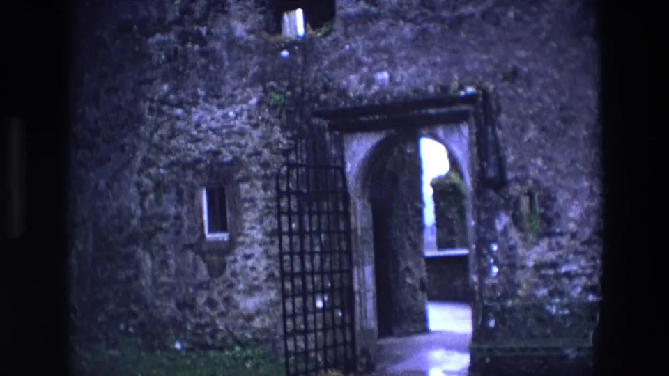 1969 Ireland 8mm frame showing the open gate and arched entrance of a weathered stone castle.