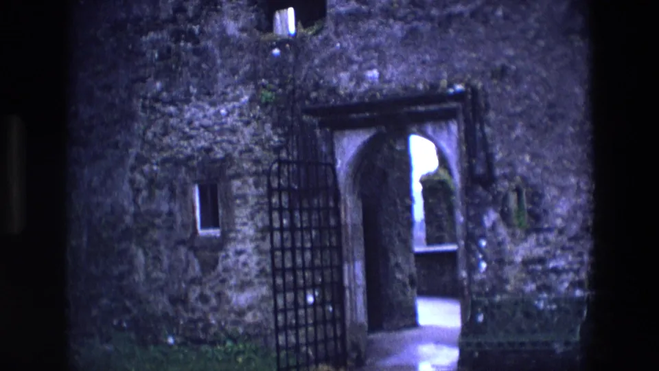 1969 Ireland 8mm frame showing a rough stone chapel entrance with a barred gate and dim arched passage beyond.