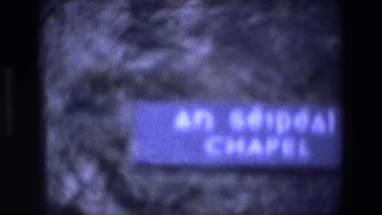 Soft 8mm close view of a blue wall sign reading An Séipéal Chapel on rough stone masonry in Ireland.
