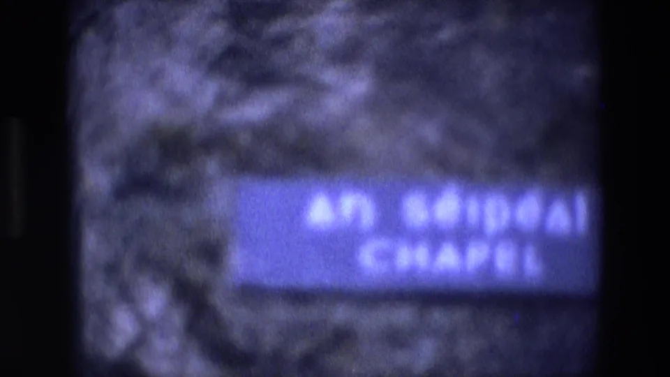 Soft 8mm close view of a blue wall sign reading An Séipéal Chapel on rough stone masonry in Ireland.