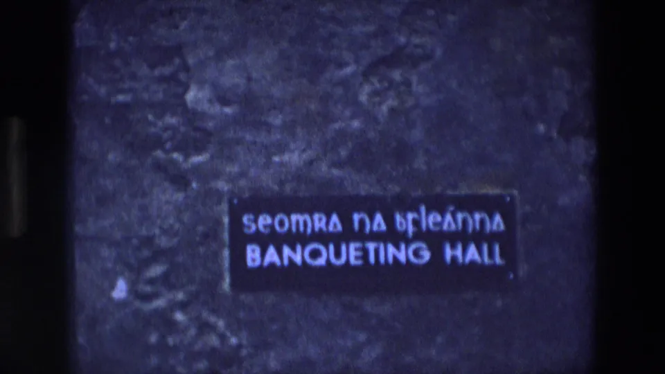 1969 Ireland 8mm frame showing Irish and English text on a banqueting hall sign against a dark wall.