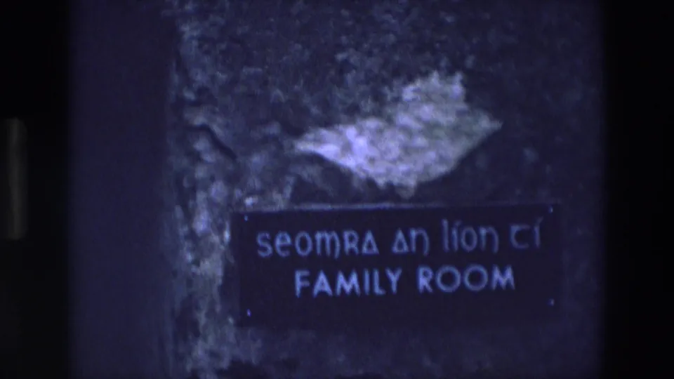 1969 Ireland 8mm frame showing a family room sign with Irish and English text on a dark textured surface.