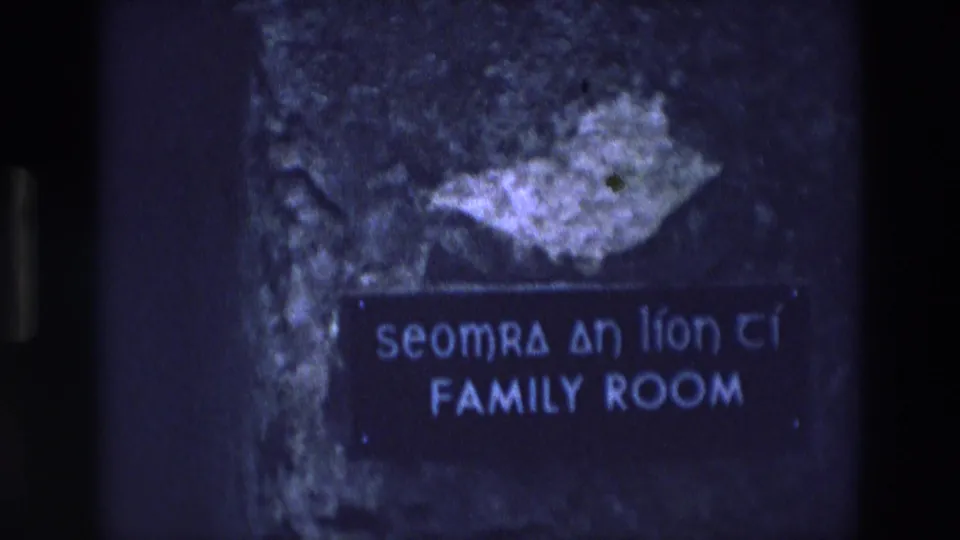 1969 Ireland 8mm frame of a bilingual family room sign, with visible grain and soft blue exposure.