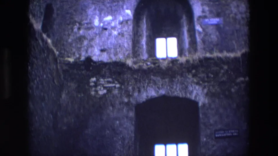 1969 Ireland 8mm view of weathered stonework, glowing narrow windows, and a large shadowed arch inside a castle.