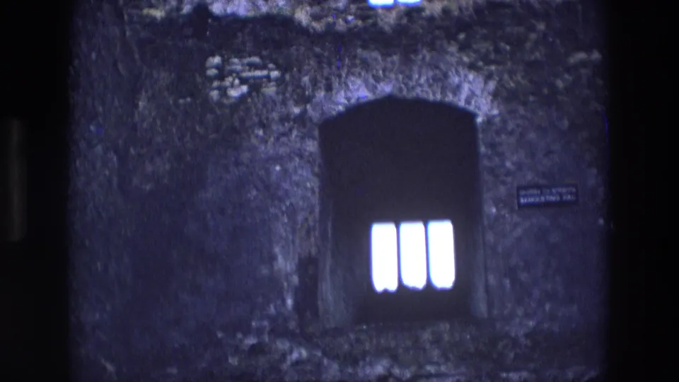 1969 Ireland 8mm frame showing rough stone masonry, a dark arched window with three bright panes, and a small banqueting hall plaque.