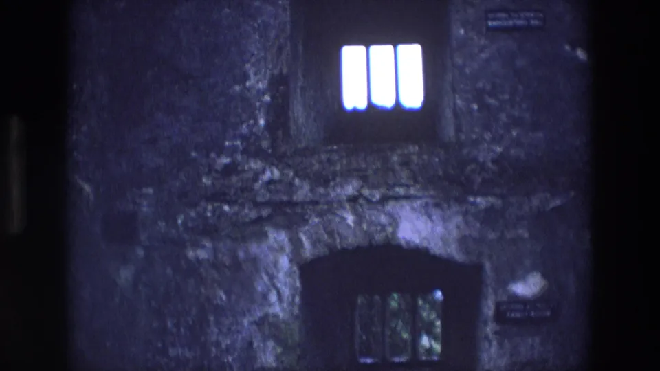 1969 Ireland 8mm frame showing an upper arched window, a lower dark opening, rough stonework, and several small wall signs.