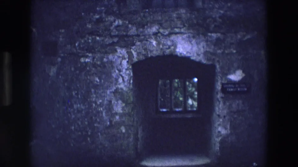 1969 Ireland 8mm frame showing a lower arched doorway or window, rough stonework, dim panes, and a small banqueting hall sign at right.