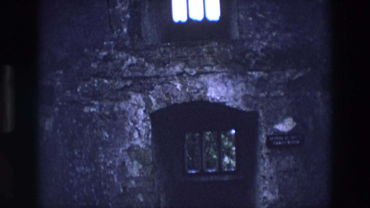1969 Ireland 8mm frame of a rough stone exterior with a narrow barred window and a small sign near the opening.