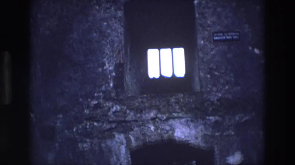 1969 Ireland 8mm frame showing a bright barred window, dark arched opening below, weathered masonry, and a small wall sign.