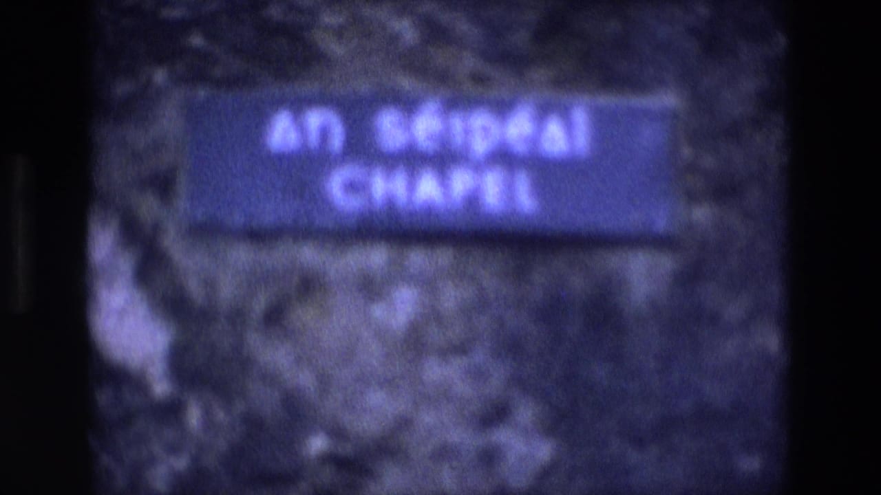 Blurred blue sign reading An Séipéal Chapel against a dark stone background.