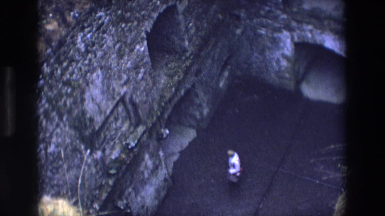 A distant visitor stands near a dark chapel or cave-like doorway in 1969 Ireland home-movie footage.