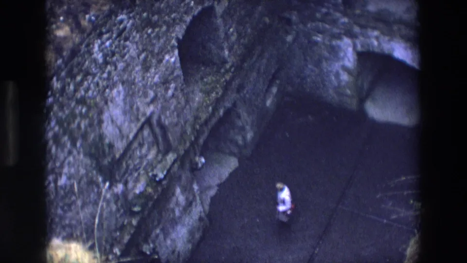 A distant visitor stands near a dark chapel or cave-like doorway in 1969 Ireland home-movie footage.