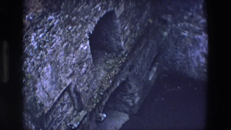 Grainy 8mm view of the chapel's rough stone entrance area, with the dark opening filling the lower frame.