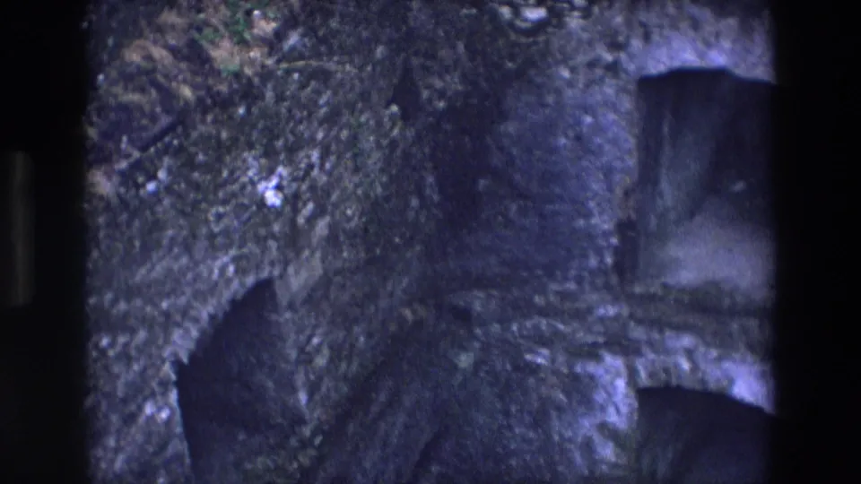 1969 Ireland 8mm frame showing a shadowed arched tunnel mouth in a moss-covered stone or rock wall.