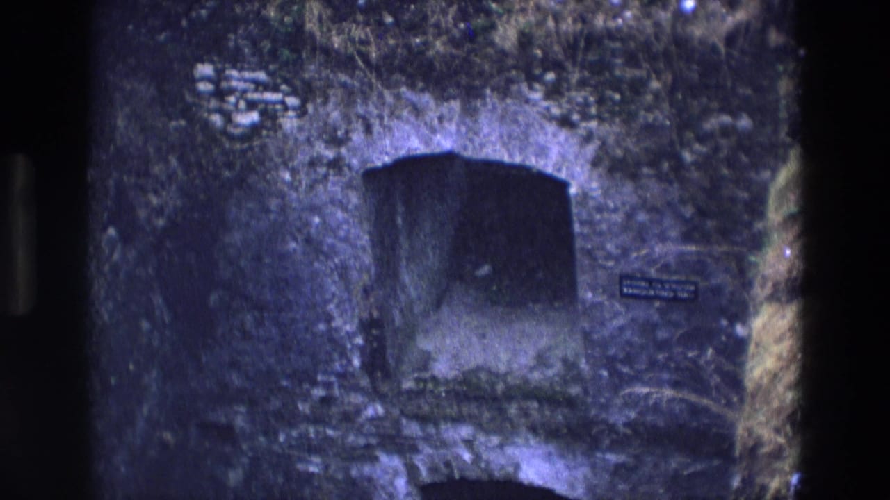 1969 Ireland 8mm frame with a dark arched passage, rough wall texture, and a small informational plaque near the entrance.