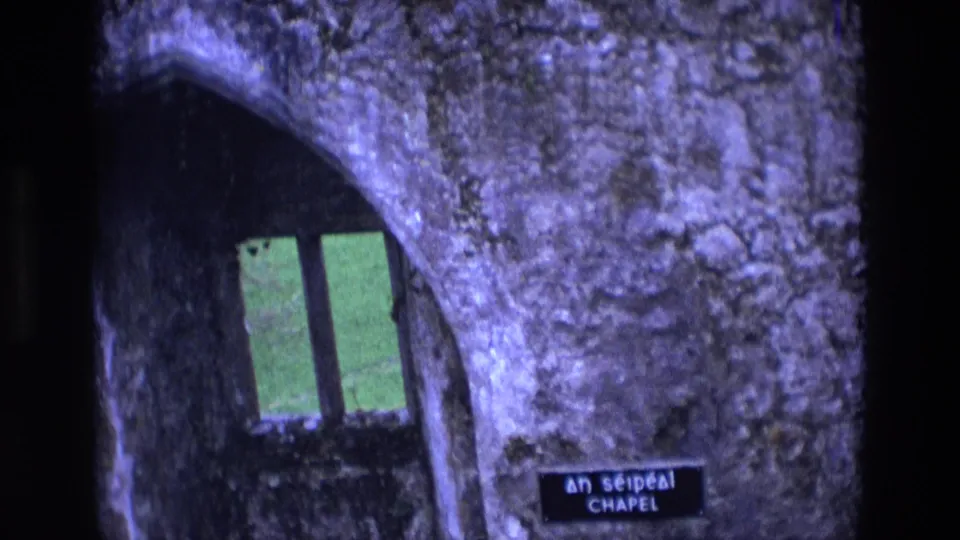 1969 Ireland 8mm frame showing a rough stone arch, narrow window, and chapel identification sign inside the ruin.