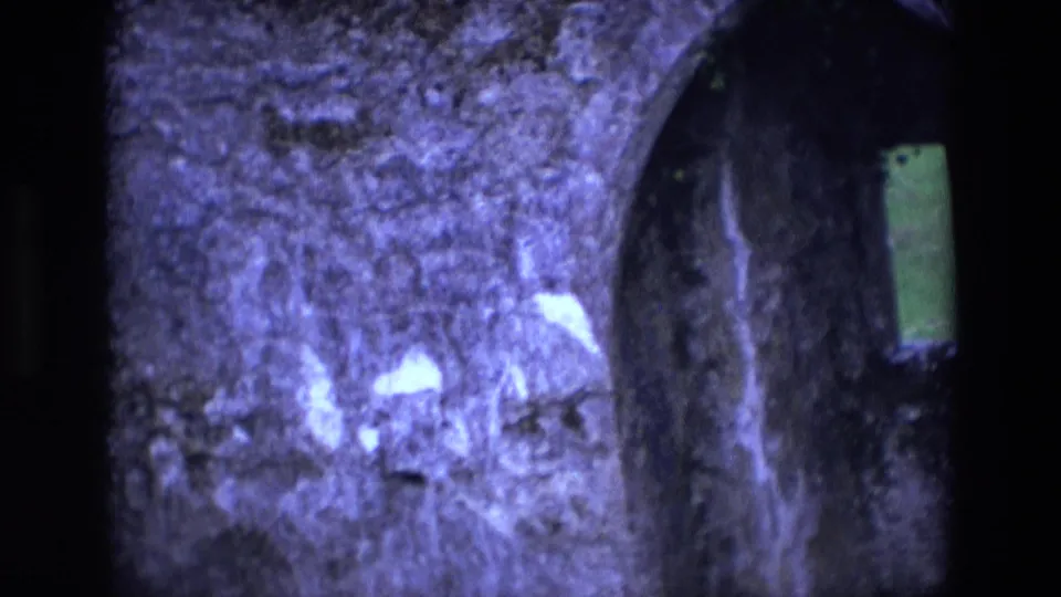 1969 Ireland 8mm frame of weathered chapel stonework and part of an arched opening with a narrow green-lit window.
