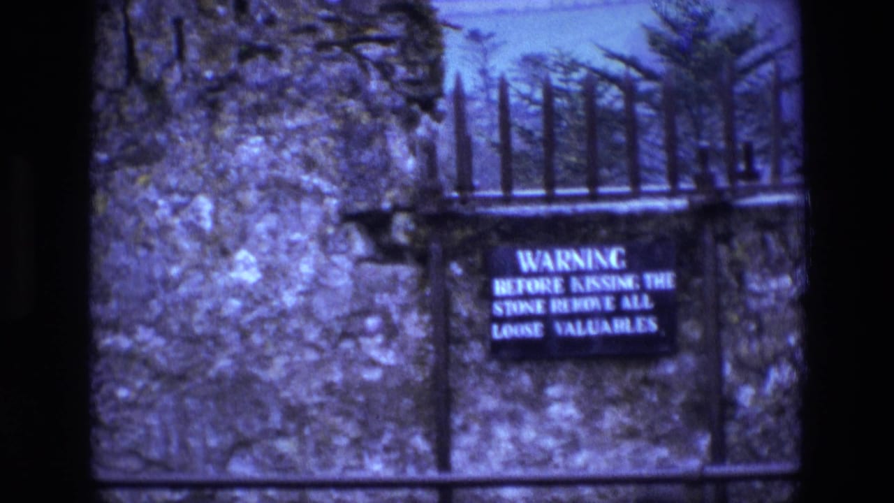 Warning sign on a stone wall with iron spikes and trees behind it.