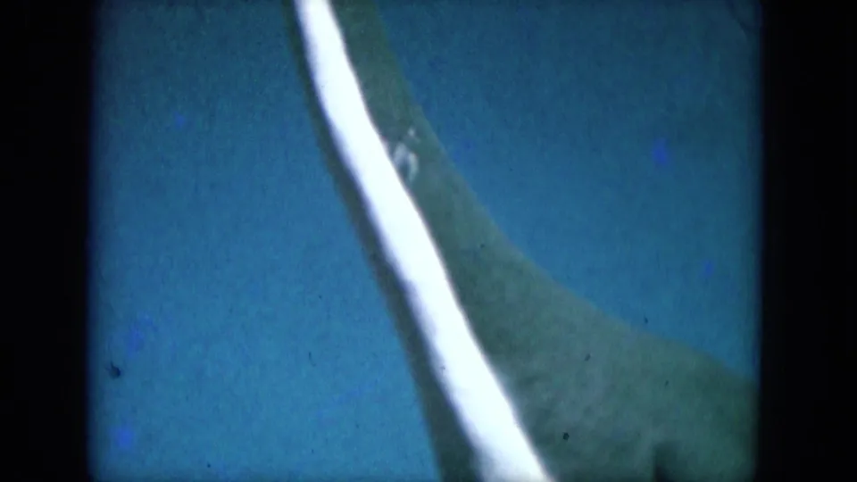 1969 Lake Canyon, Arizona 8mm frame showing an unclear green form with a white stripe against a blue field.