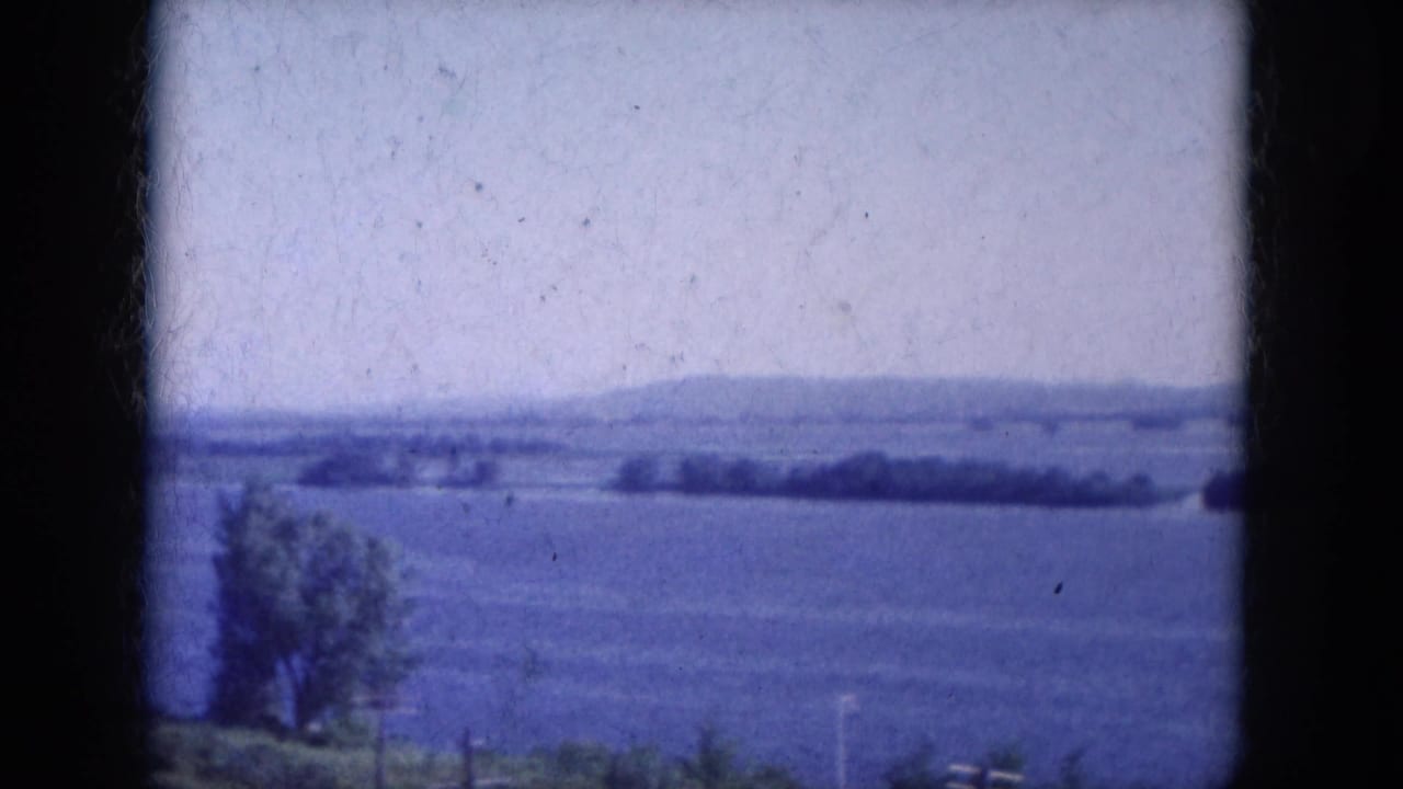 Wide blue-tinted view across open water toward distant shoreline and low hills.