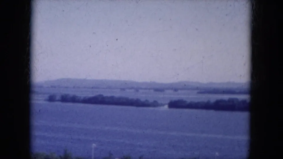 1969 8mm frame of Lake Canyon, Arizona, looking over a broad body of water toward low distant hills and a narrow shore.