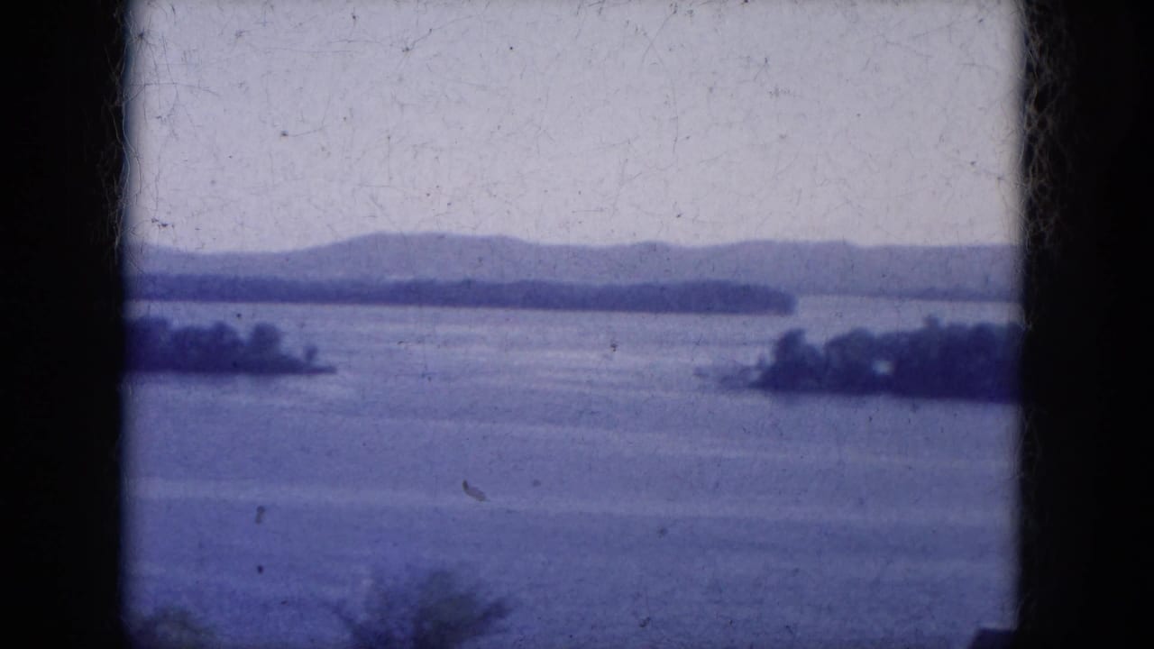 Wide lake view with islands, distant hills, pale sky, and dark 8mm frame borders.