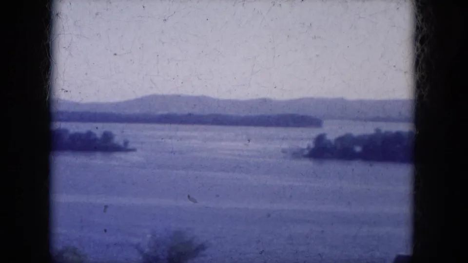 1969 8mm view of an Arizona lake with low islands across the water, distant hills, a pale sky, and visible film-frame borders.