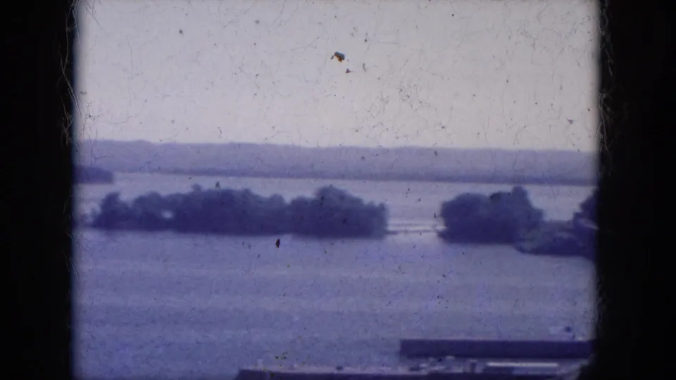 Soft 1969 home-movie frame of Lake Canyon, Arizona, showing islands on the water, distant hills, pale sky, and a central film border.