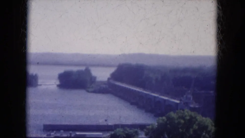 1969 8mm lakeside view in Arizona with islands, a low bridge or causeway, shoreline vegetation, distant hills, and soft color fading.