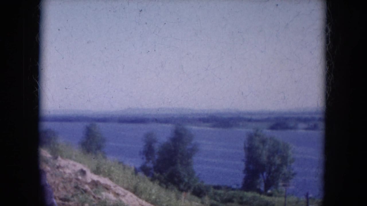 1969 Lake Canyon, Arizona frame with wide blue water, a green bank, scattered trees, and a soft distant horizon.