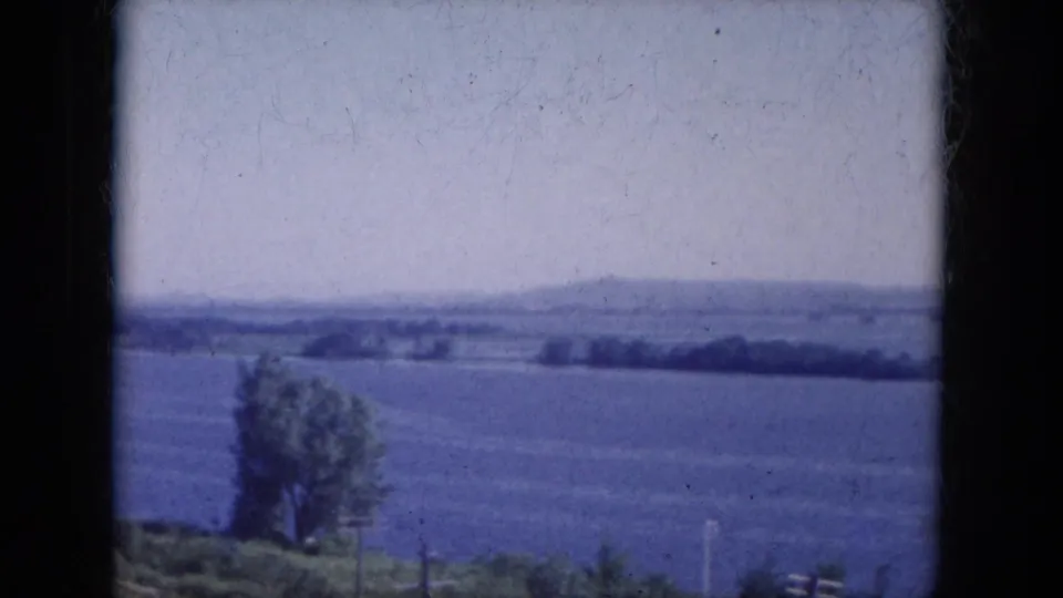 1969 Lake Canyon, Arizona frame with open blue water, a lone riverside tree, fence posts, and a distant low shoreline.