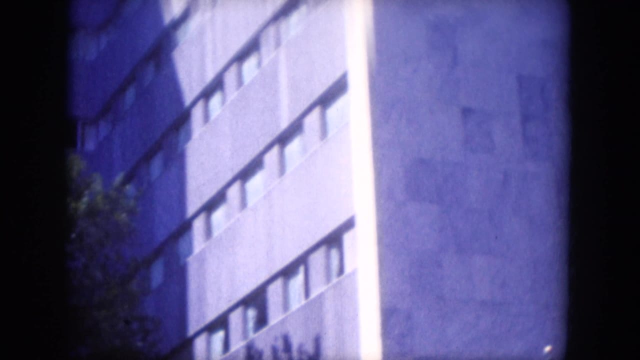 Concrete building corner with horizontal windows, trees, and dark film-edge framing.