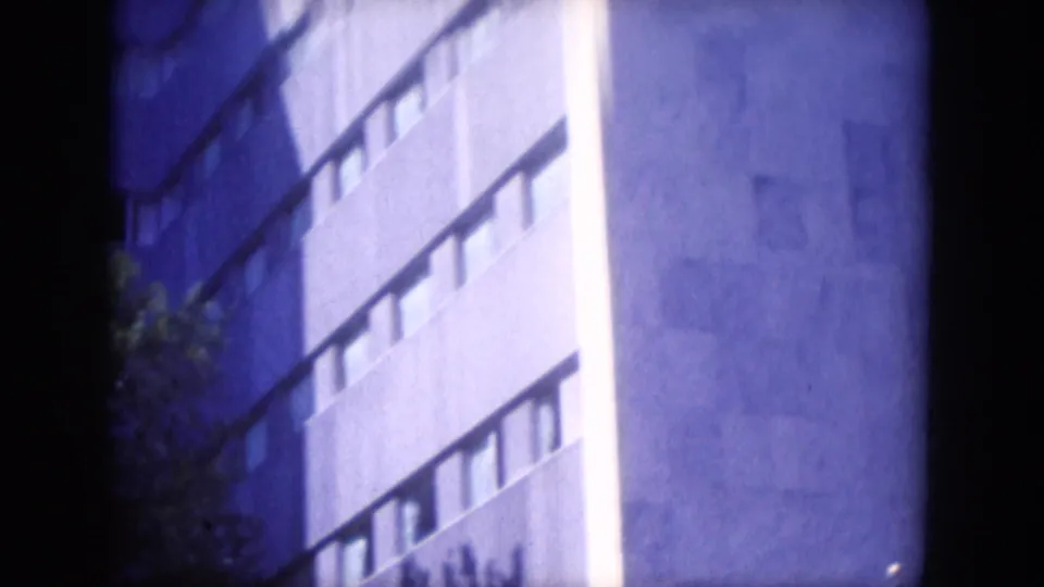 1969 Lake Canyon, Arizona 8mm frame showing a concrete building corner with narrow windows and trees at the edge.
