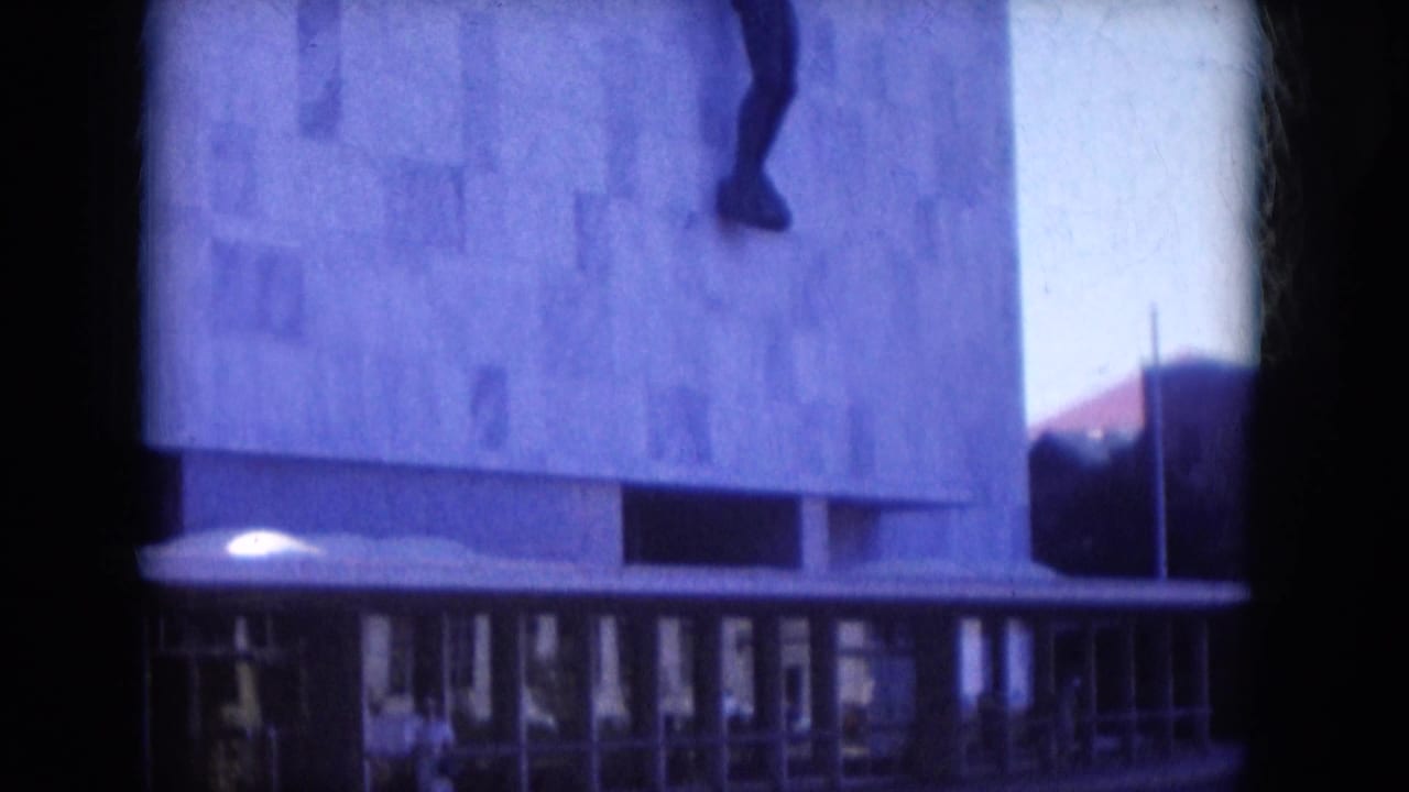 1969 Lake Canyon, Arizona frame showing a concrete facade, entrance glazing, and part of a dark wall-mounted figure above.