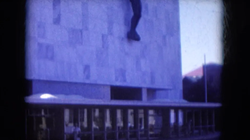 1969 Lake Canyon, Arizona frame showing a concrete facade, entrance glazing, and part of a dark wall-mounted figure above.