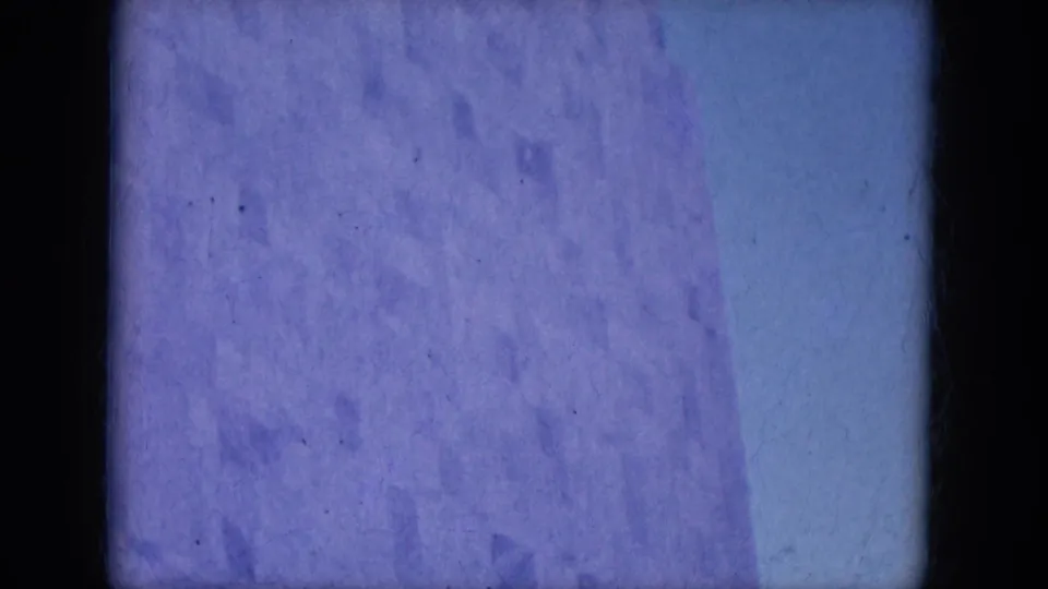 Blue-tinted, largely obscured 8mm frame with film borders and visible surface marks before the street scene appears.