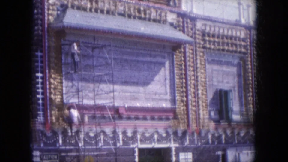 The final frame shows scaffolding against the decorated exterior, with a small worker or pedestrian near the facade and patterned trim around the windows.