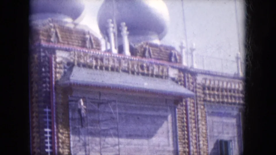 1969 8mm frame from Lake Canyon, Arizona showing white onion-shaped domes above a decorated facade with scaffolding and a worker.