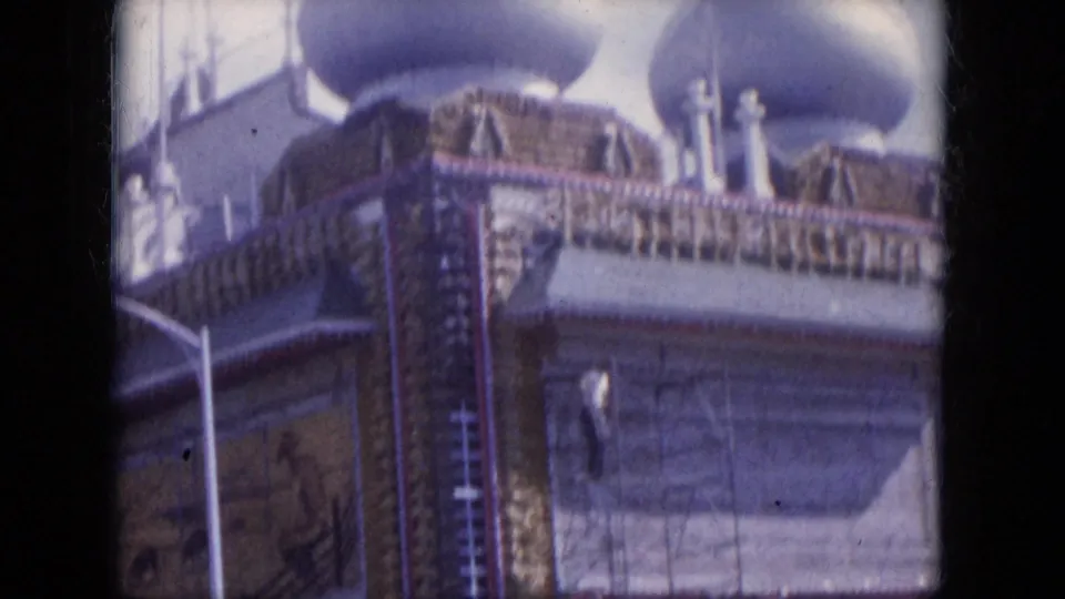 1969 8mm view in Lake Canyon with ornate domes, scaffolding, a streetlight, and a worker positioned on the building exterior.