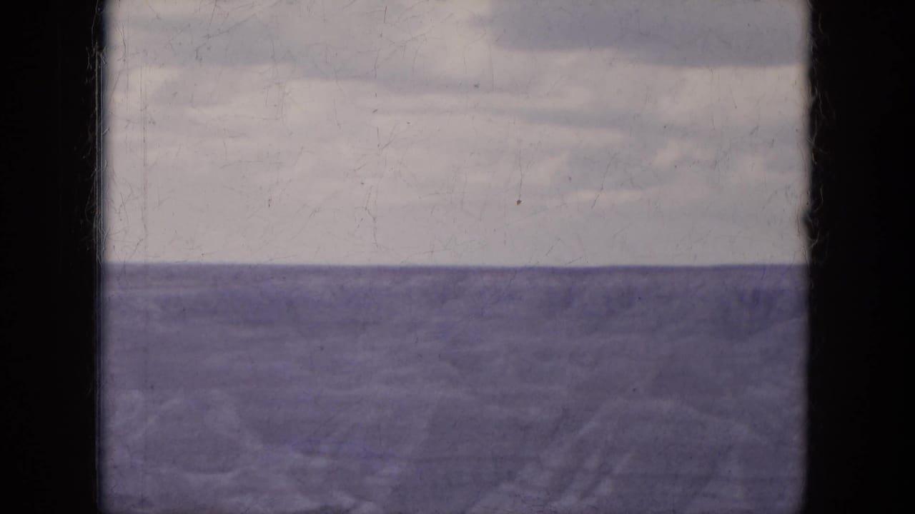 Cloudy sky above a broad water horizon, framed by dark film borders.
