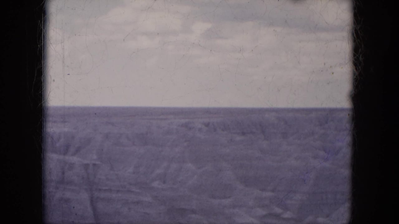 Flat water horizon under a pale sky with visible film wear and border edges.