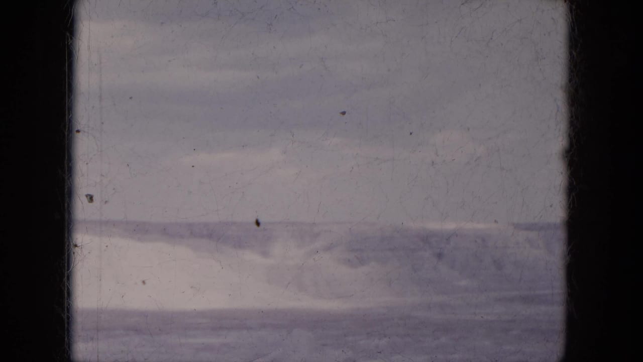 Distant hills and gray sky seen through a dark vehicle window frame.